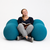 Person sitting on a blue Squeeze Me Deep Pressure cushion reading a book against a white background