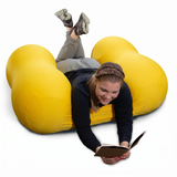 Person lying on a yellow Squeeze Me Deep Pressure cushion reading a book