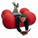 Person lying on a red Squeeze Me Deep Pressure cushion reading a book