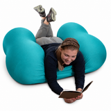 Person lying on a teal Squeeze Me Deep Pressure cushion reading a book