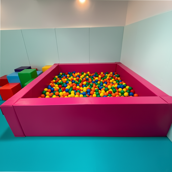 Pink ball pit with colorful balls in a room with light blue walls and floor.