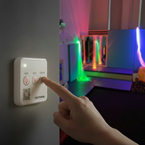 Hand pressing a wall-mounted light control device with colorful lights in the background